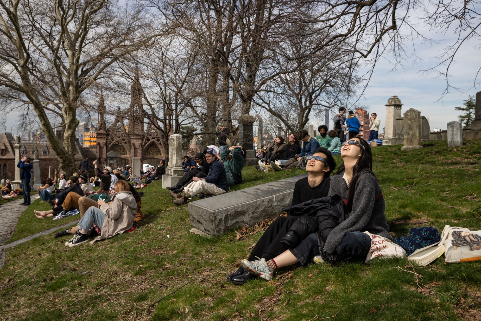 Attendees in eclipse glasses watching the solar eclipse from the grassy hills of Green-Wood Cemetery, April 2024